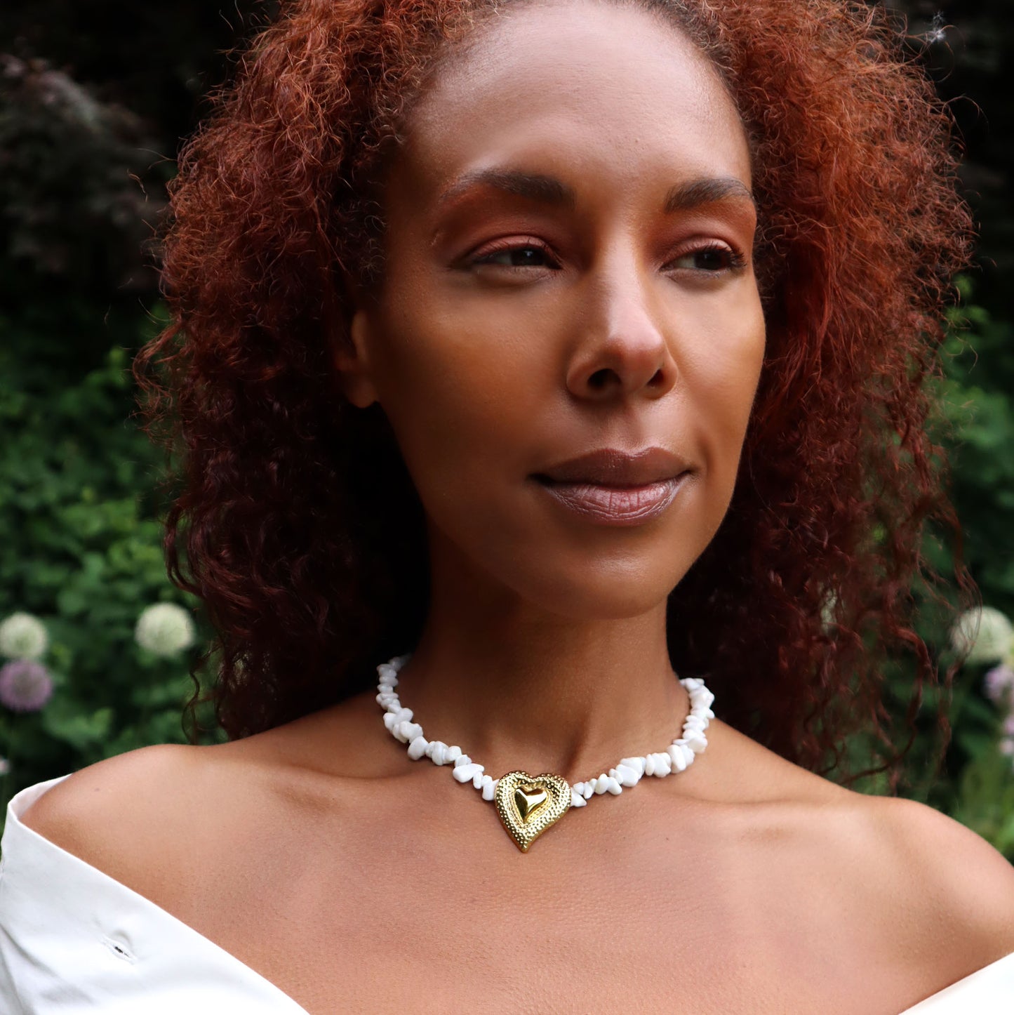 Necklace featuring a strand of white shell chips and a bold, gold-toned double heart pendant