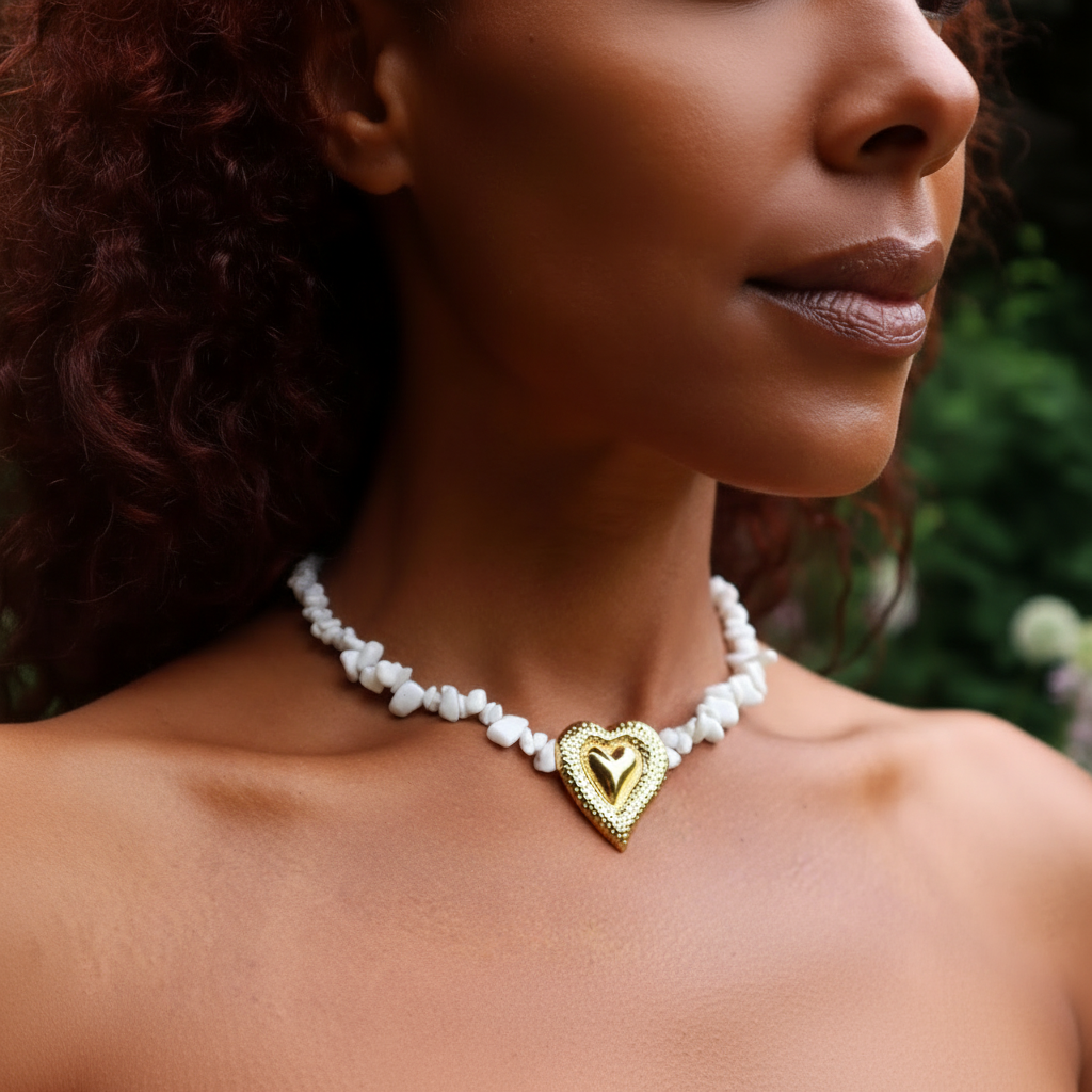 Necklace featuring a strand of white shell chips and a bold, gold-toned double heart pendant